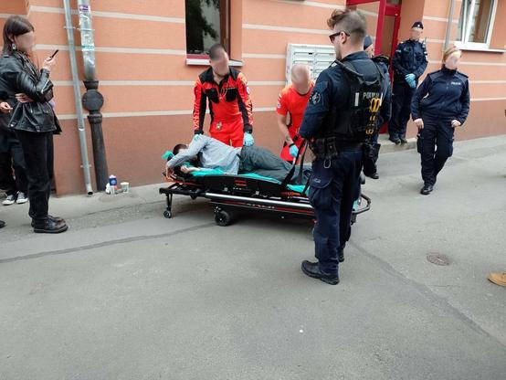 Zdjęcie przedstawia przeniesienie przez ratowników medycznych aktywisty do karetki. Wokół policja.