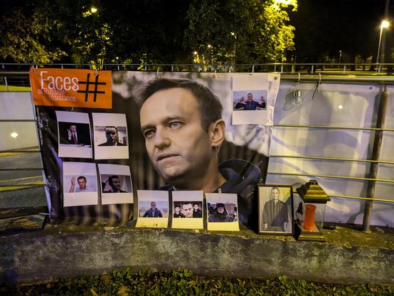 A signboard in the park opposite the Russian and Ukrainian Embassies in Riga, Latvia. The text reads "Faces of Russian Resistance" n English with a misplaced # for a hashtag. Navalny's face is large and centered. Smaller mages of eight others surround him.