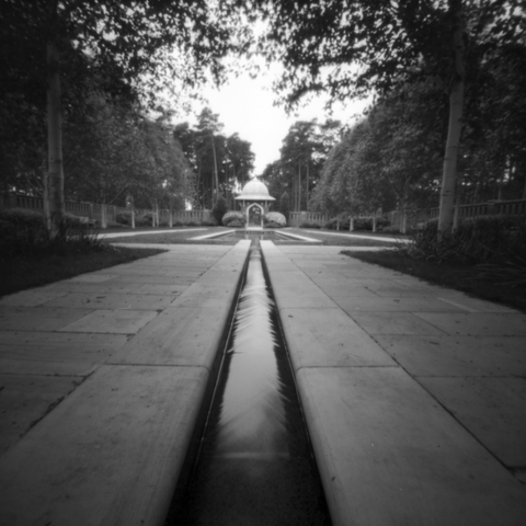 Photograph with camera at ground level looking down a watery channel leading to a shallow pond in the middle of a peace garden.