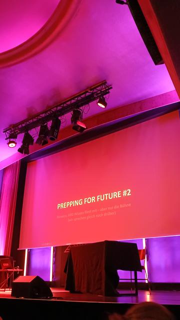 Zu sehen ist eine Leinwand, die rötlich beleuchtet wird. An die Wand wird der Text "Prepping for Future #2" geworfen.