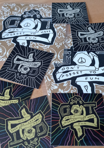 auf dem Tisch liegen 2 Spokecards und 2x3 Sticker mit dem Logo vom GameOfToiletpaper. Die Sticker sind einmal Silber auf Schwarz, das andere Set ist Gold mit Regenbogen-farbener Aura auf schwarzem Hintergrund
