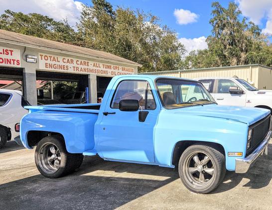 Bright blue pickup truck in decent condition in a parking lot of an old auto repair shop.