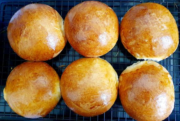 Again, top down photo of 6 bread buns, they were brushed with egg yolk, so they have a darker golden appearance. These are flatter buns than the other ones. They are soft and squishy and I cut into one to check the crumb and it looks baked and lovely.