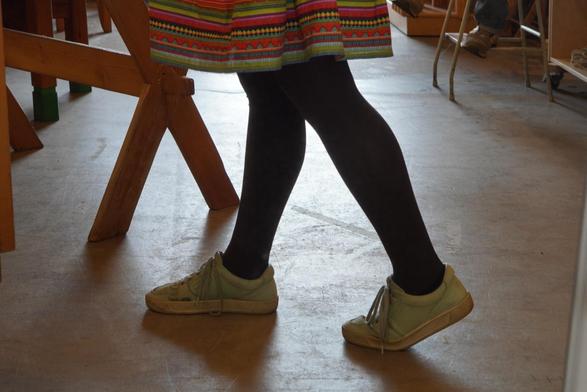 My legs and shoes in the middle of a step. The bottom vit of a skirt can be seen going almost down to my knees. There's furniture in the background of the image.