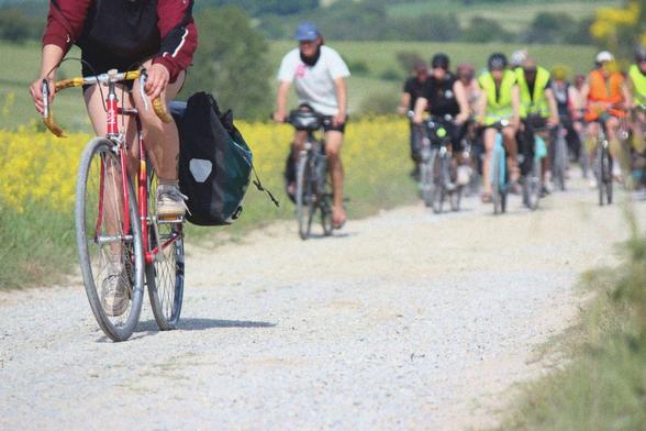Foto von fahradfahrenden Menschen auf einem staubigen Kiesweg von vorne.