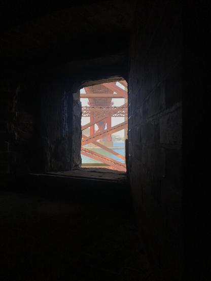 Most of the frame is black. In the middle is an almost-rectangular window opening through which is shown the underside of the Golden Gate Bridge and a bit of blue water. Photo taken at Fort Point under the south end of the bridge.