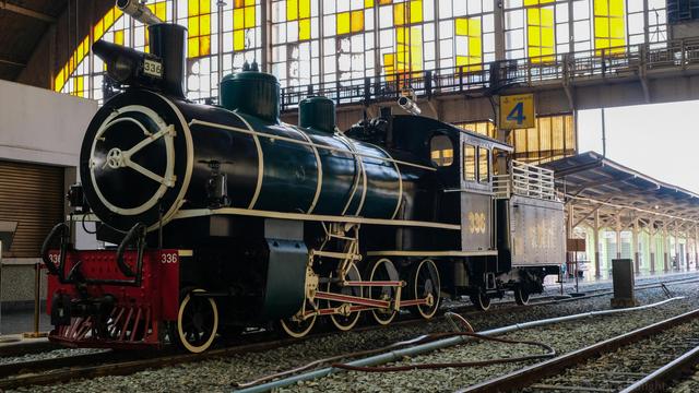 A parked early 20th century / late 19th century train engine inside the roof covered train station.