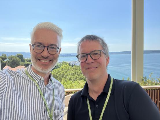 Me (left) and Axel, smiling for a selfi above the adriatic sea. @lysander07 The image features two men standing close together, smiling at the camera. They are both wearing glasses and lanyards with green tags. The man on the left has white hair and a beard, wearing a striped shirt, while the man on the right has gray hair and is wearing a black polo shirt. They are positioned in front of a large window that offers a scenic view of a body of water, likely a lake or sea, with lush green trees and a clear blue sky in the background. The setting appears to be a sunny day, with the men standing on a balcony or terrace, enjoying the view.

Provided by @altbot, generated privately and locally using Ovis2-8B

🌱 Energy used: 0.148 Wh