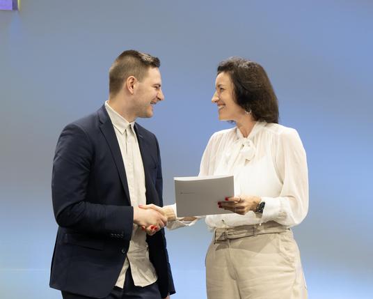Bundesforschungsministerin Dorothee Bär (r.) beglückwünscht David Rutkevich (l.) für den Preis für die interdisziplinärste Arbeit: Der Jungforscher hat ein KI-Modell entwickelt, das Tumore auf MRT-Aufnahmen besser als frühere Systeme erkennt.