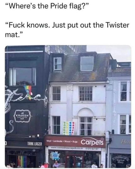 A row of buildings along a city street, one with a Pride flag hanging from a window. The building next door has a...Twister mat?!

"Where's the Pride flag?"

"Fuck knows. Just put out the Twister mat."