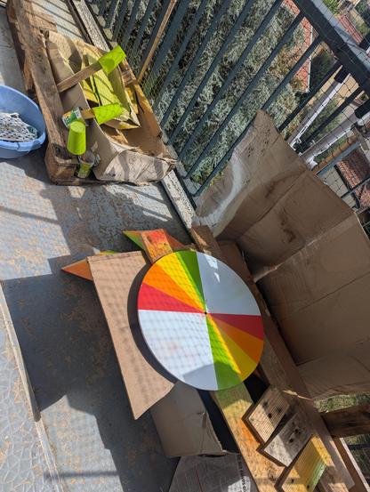 On voit un disque en bois d'environ 50cm de diamètre.
La moitié est peinte en quartier de camembert, il y a du vert, du jaune, du orange et du rouge. Le fond qui n'est pas encore peint est blanc