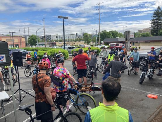 A crowd of roughly 40 cyclists in a parking lot under a blue sky