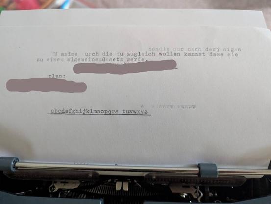 Auf einem Blatt Papier, eingespannt in eine Schreibmaschine der Text:
handle nur nach derjenigen Maxime durch die du zugleich wollen kannst, das sie zu einem allgemeinen Gesetz werde.