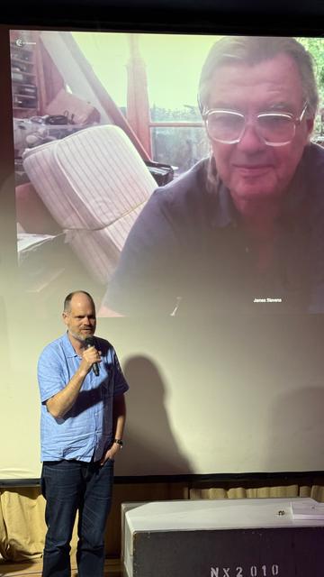 Julien Priest talking into microphone while James Stevens looks down from the screen.