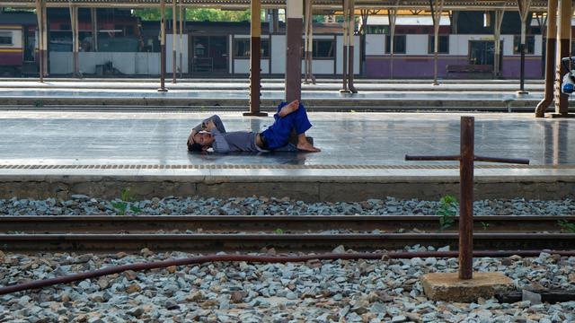 A train station worker taking a break laying flat on one of the train stone platform at a very quiet train station