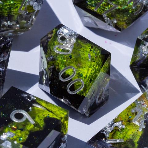 A 10-sided die in the middle, surrounded by other TTRPG dice. The die contains green snake and dark glittery swirls and is inked in silver.