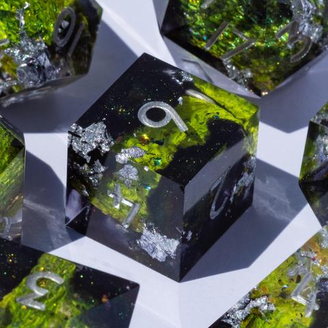 A 6-sided die in the middle, surrounded by other TTRPG dice. The die contains green snake and dark glittery swirls and is inked in silver.