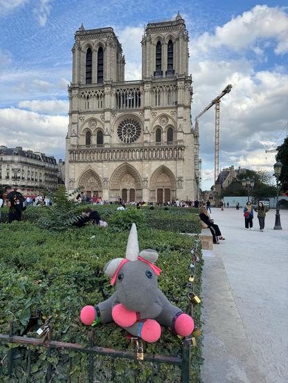 Alma, a grey unicorn plushie, sitting on bushes in front of Notre Dame.