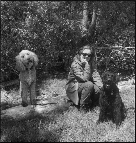 A woman, a labradoodle and goldendoodle pose on a log. As taken on black and white film.