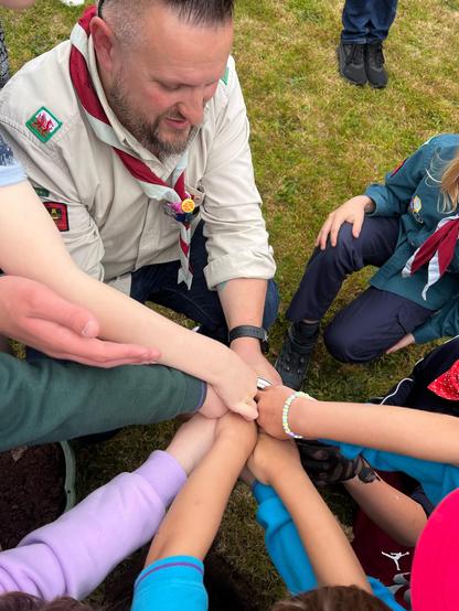 Out Group Lead Volunteer with five arms belonging to Young People stuff things into a time capsule.