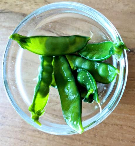 8 Mange tout in a small bowl of glass on a wooden table.