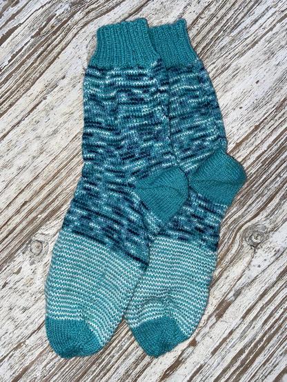 Türkisfarbene gestrickteSocken, bei denen ich in jeder Runde das Knäuel gewechselt habe. Nachdem mir die melierte Wolle ausging, habe ich sie mit weißer Wolle ersetzt.