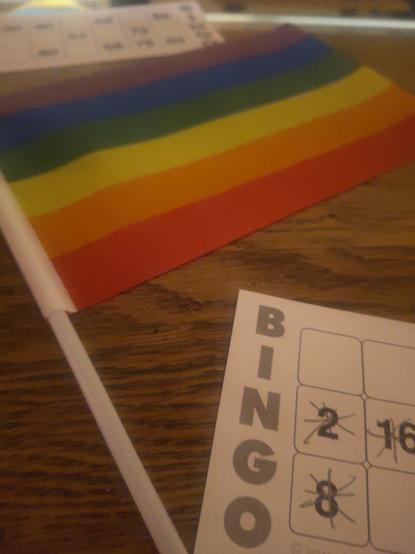Eine Regenbogenfahne neben einer Bingokarte auf einer Holztheke.