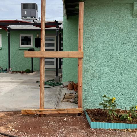 Two post with cross beams in front of a green house.
