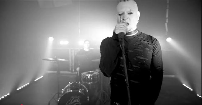 Ein Standbild aus dem Teaser-Video der Band Hard&Spades. In dem Schwarz-Weiß-Bild spielen die beiden Musiker in einem Club vor hellen Scheinwerfern. Im Vordergrund hält der blasse Sänger mit schwarzem Augen-Make-up das Mikrofon fest und singt. Im Hintergrund spielt der Schlagzeuger.