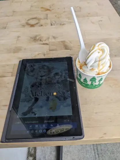 Soft serve ice cream on a table with a tablet showing Management of an Novice Alchemist