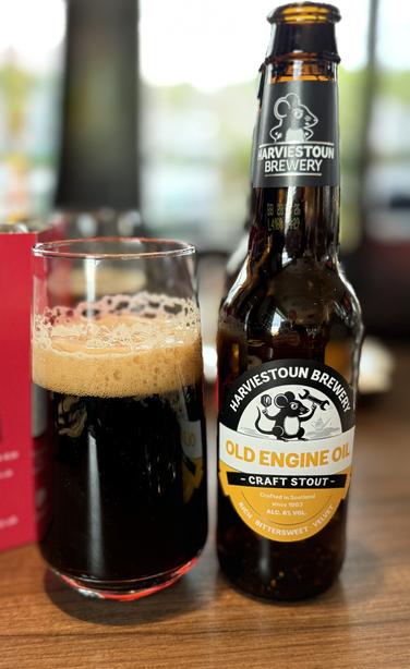 A glass of dark beer with a bubbly tan head next to the brown bottle with a yellow and white label and a mouse with a monkey wrench