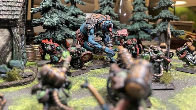 A giant blue humanoid screeches as it breeches a tree line towards a team of skaven globadiers. It’s blue skin barely covered with leather wrapping and rusty armour. A skirmish team of orcs accompany its charge.