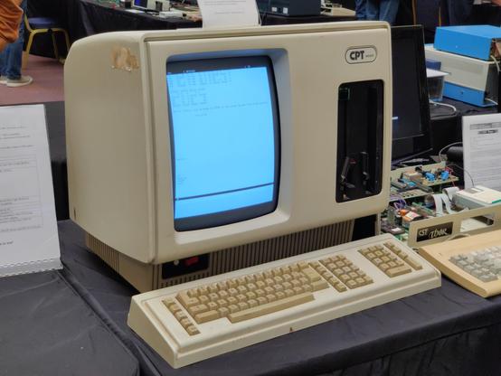 A photo of a very tall and imposing cream-coloured terminal with detachable keyboard. The monitor is portrait orientation, in the left half of the case. The right half contains two 8 inch floppy drives in vertical orientation. The keyboard is a large wedge with a nonstandard layout. There are no modifier keys where you'd expect to find control, alt and meta, and where you'd expect to find the home/end and cursor blocks, there are two vertical blocks of 1x5 and 3x5 keys. To the right of that is a numpad and another column of four keys.