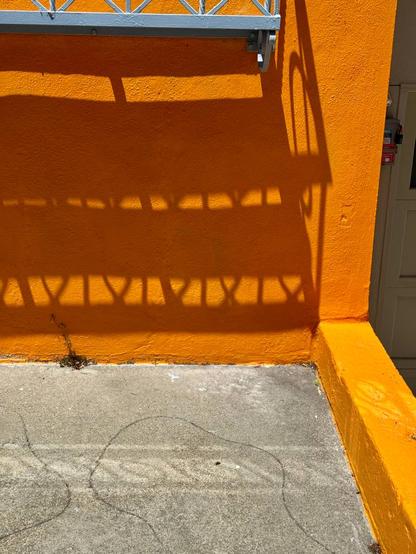 The side of a house with orange walls and a concrete driveway. There is a shelf under the front windows that is casting a shadow on the wall beneath it. This shadow was used as inspiration for my drawing of several orks, but this is the original photo.