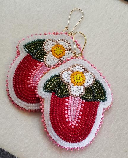 a pair of beaded earrings made by kiamichi representing halved strawberries in red and pink with their white and yellow flowers and green leaves on top