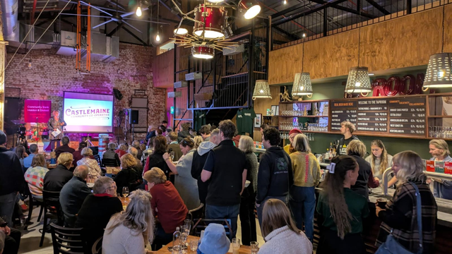 Crowd of people at the Taproom in Castlemaine. Someone is speaking on stage, and there's a projector showing the Castlemaine Community Co-operative's logo.
