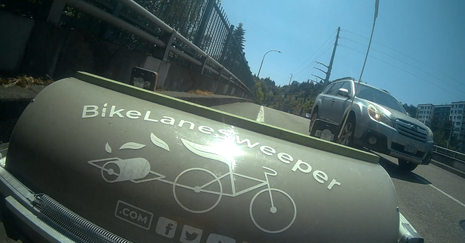 white subaru passing the bike lane sweeper which barely fits in some under-spec lanes to begin with