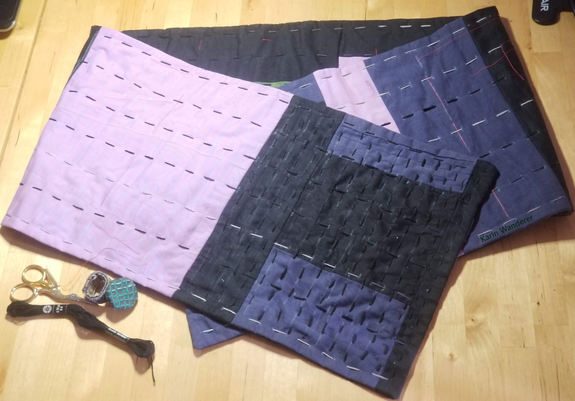 Photo of a patchwork scarf in purple, blue, & black with lines of kantha running stitch covering about 1/7 of it.
