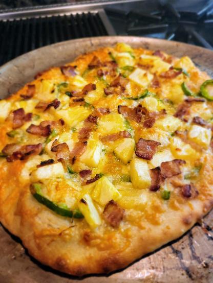 Homemade pizza topped with mozzarella cheese, bacon, pineapple, and jalapeños.