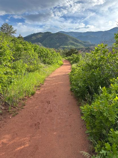 A path leads through the center of the picture towards the mountains. Lush greenery lines both sides of the trail.