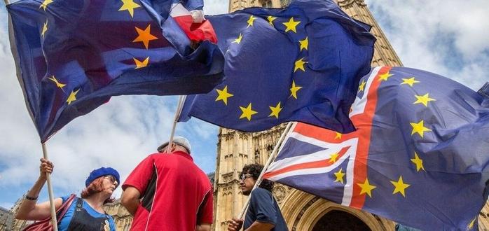 A man holding a flag, with a European flag draped over his back, standing proudly.