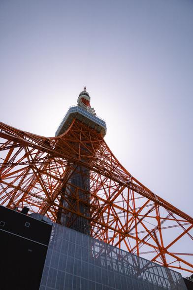 photo of the side of the tokyo tower, taken in a sharp angle from below, with the sun shining behind the main floor