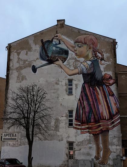 Mural with a girl who waters a real tree which has no leafs