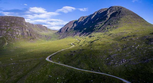 A road snakes up a steep sided green valley.