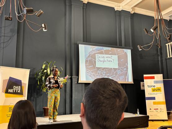 Die Künstlerin Esther Mwema auf einer Bühne vor einem ihrer Kunstwerke.