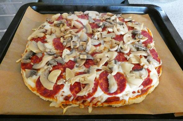 Eine Pizza auf einem Backbleck,welches mit Backpapier ausgelegt ist.