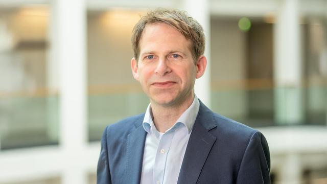 Prof. Peter Kühnen: Mann im mittleren Alter mit kurzen blonden Haaren. Er trägt ein weißes Hemd mit einem grau-blauen Jackett. Der Hintergrund ist unscharf  © Charité | Maria Streltsova
