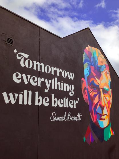 Professionally painted on a black gable wall is the text "Tomorrow everything will be better - Samuel Beckett", alongside a colourful stylised portrait of the playwright.