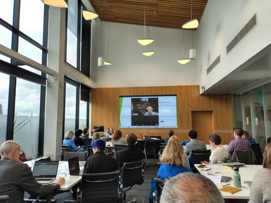 Photo of CoLIS 2025 doctoral workshop seminar room. Focus of the image is Prof. Thomas Wilson on screen, presenting remotely. Doctoral conference delegates can been seen sitting at tables.