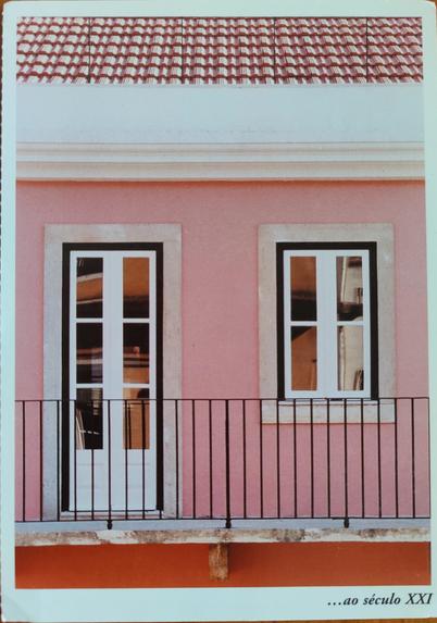 A imagem mostra a fachada, recentemente renovada, de uma casa com características arquitectónicas típicas do século XIX. A parede da casa está pintada  de cor-de- rosa vivo. A porta, de caixilharia de alumínio pintada de branco e seis vidros espelhados. Ao lado da porta, uma janela  também de caixilharia em alumínio pintada de branco e quatro painéis de vidraças espelhadas. Em primeiro plano, um gradeamento muito simples em ferro forjado escuro parece definir uma área privada de acesso. A cobertura é recente e de telha avermelhada. As vidraças reflectem algumas áreas dos edifícios defronte, em tons de cor-de-laranja, castanho-escuro e branco.